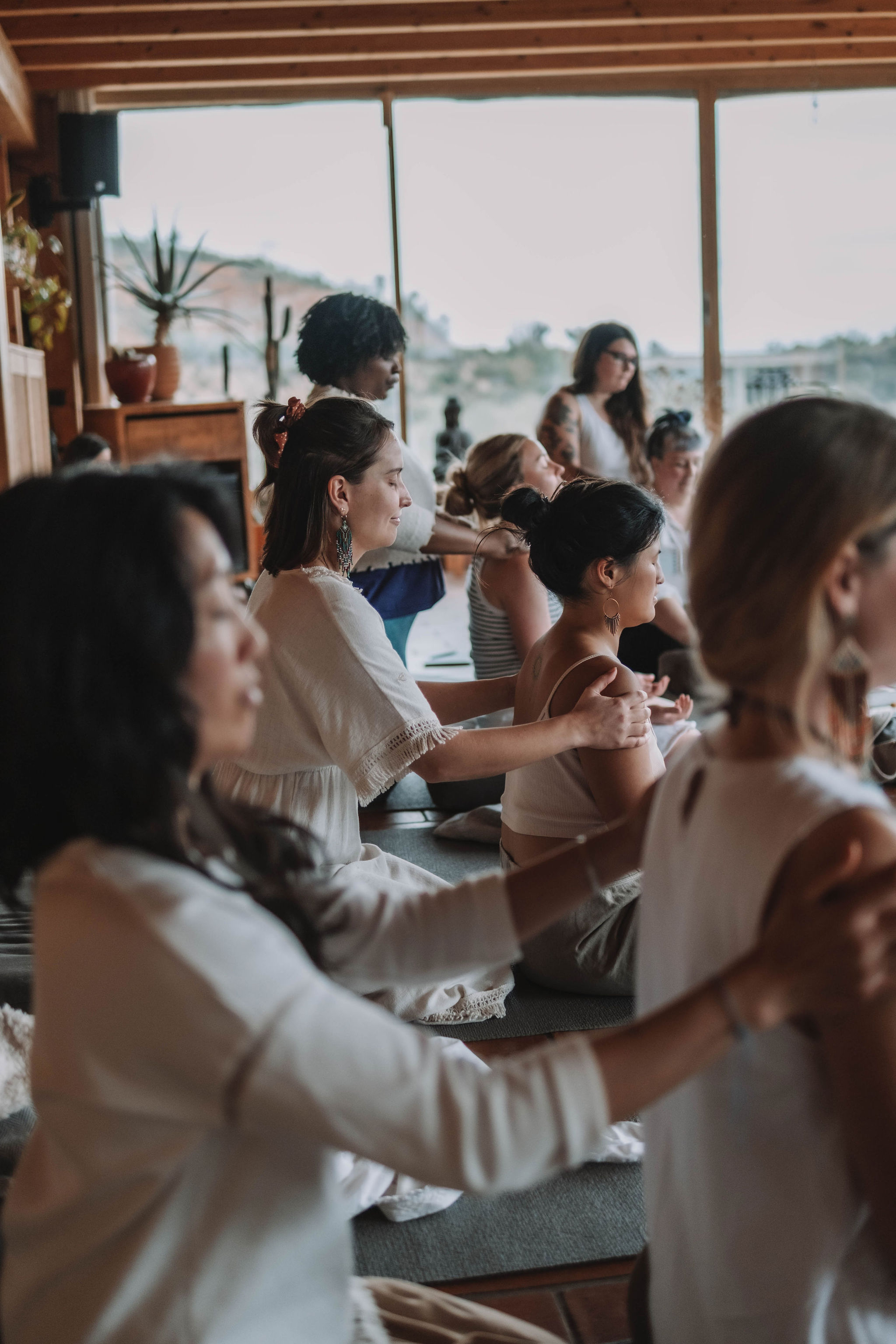 Group of diverse women seated indoors, giving each other shoulder massages in a calm, meditative environment.