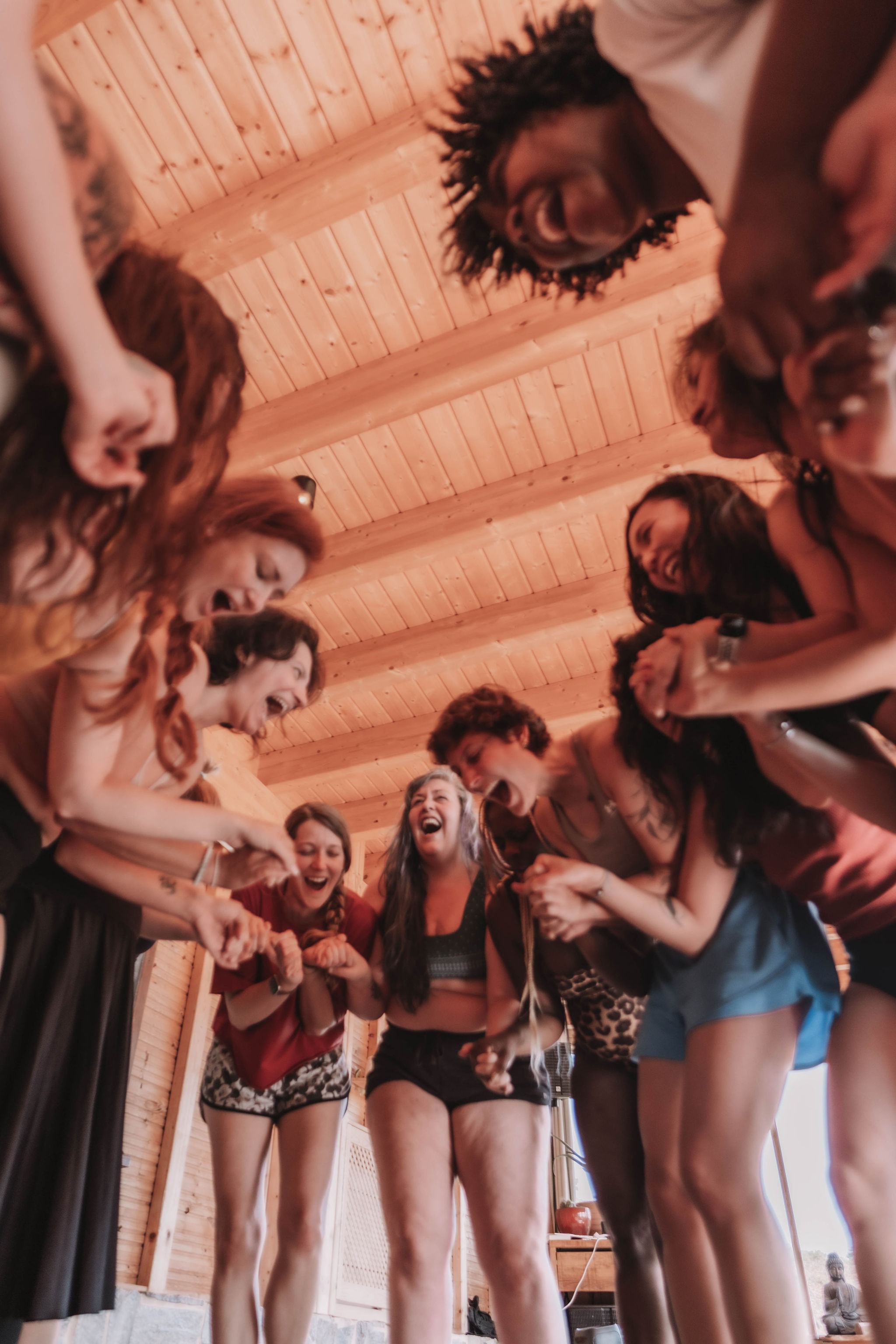 Group of diverse women standing in a wooden room, holding hands and laughing together.