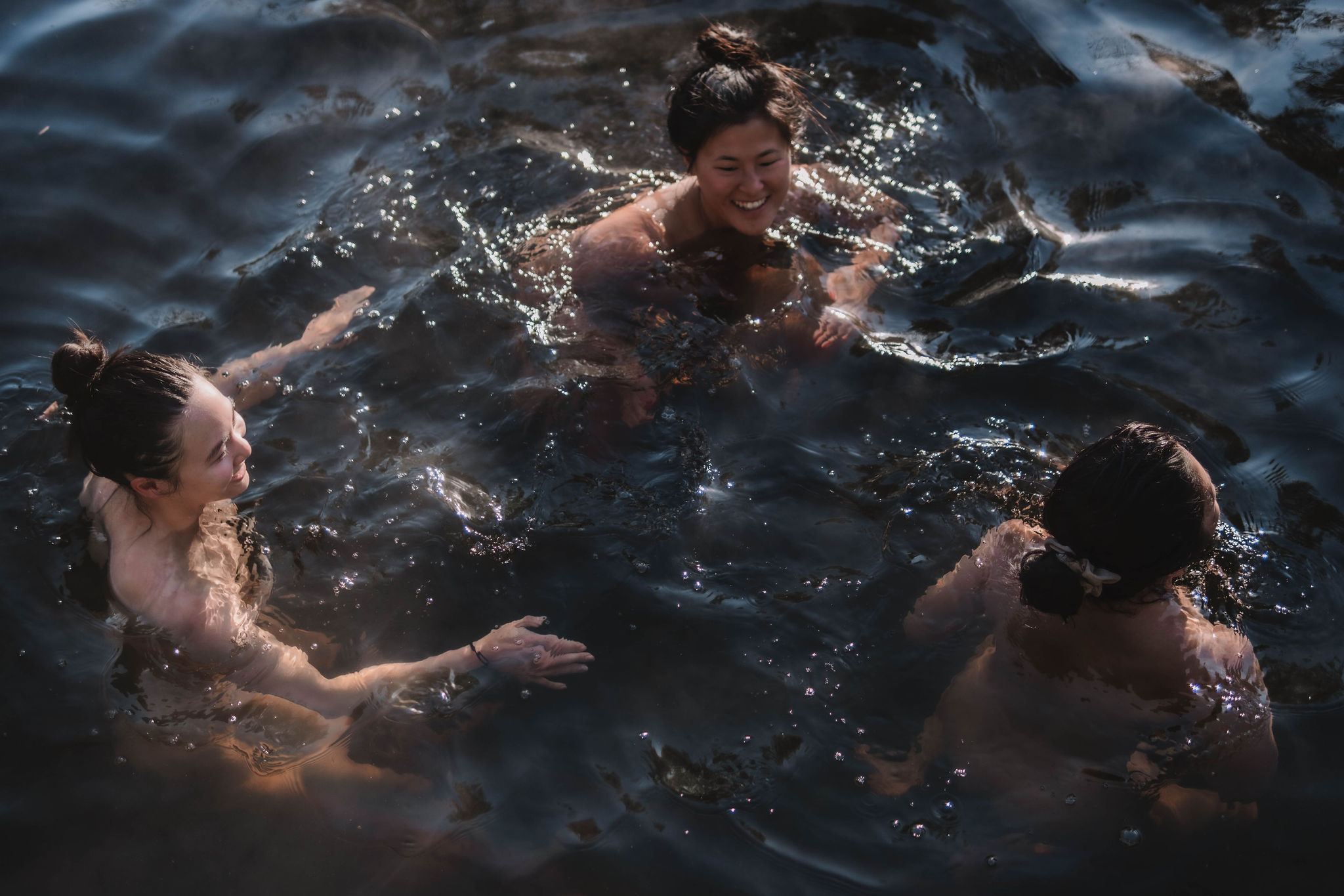 Three women with hair in buns smiling and swimming in dark water.
