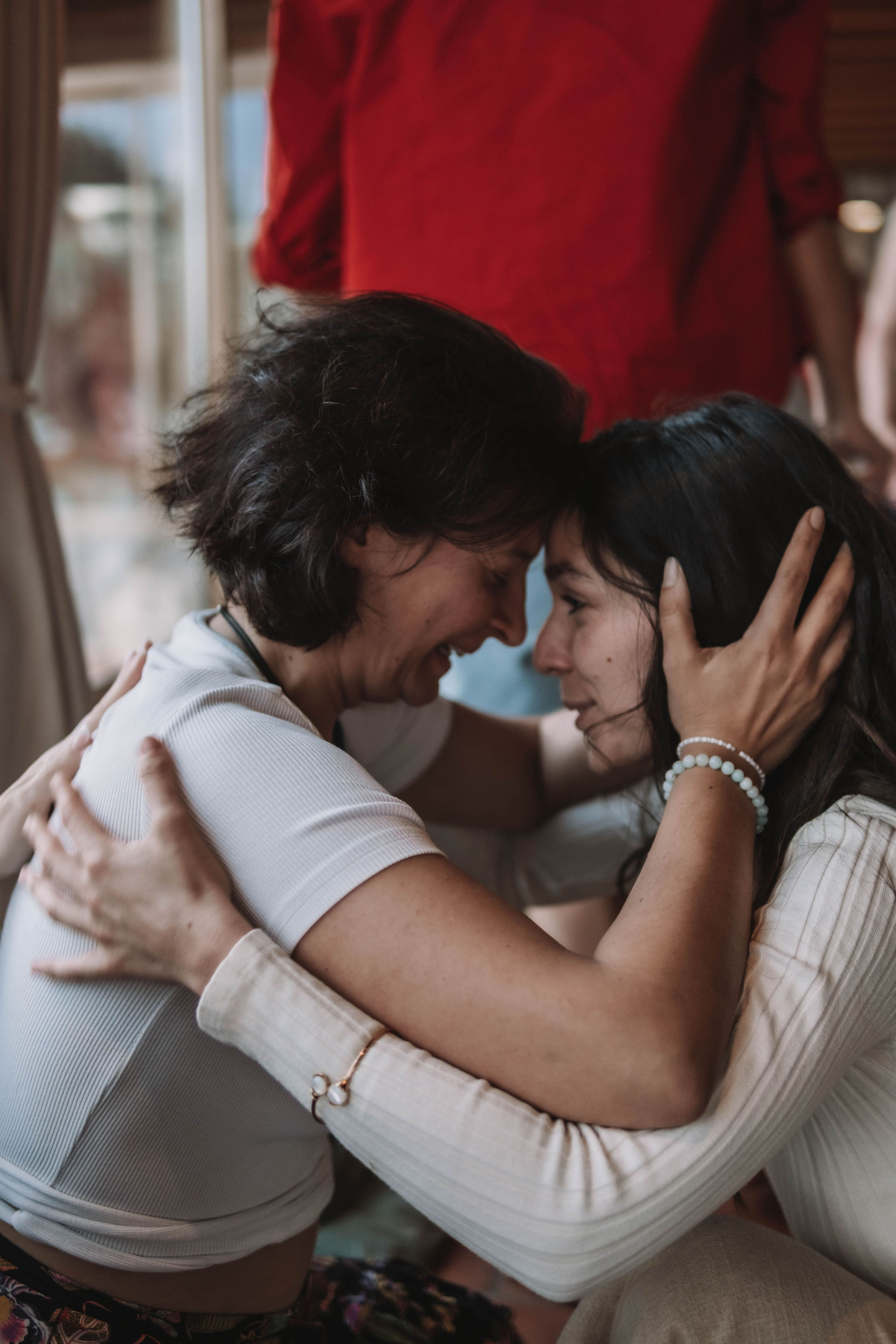 Two women embrace closely with foreheads touching, sharing an emotional moment indoors.