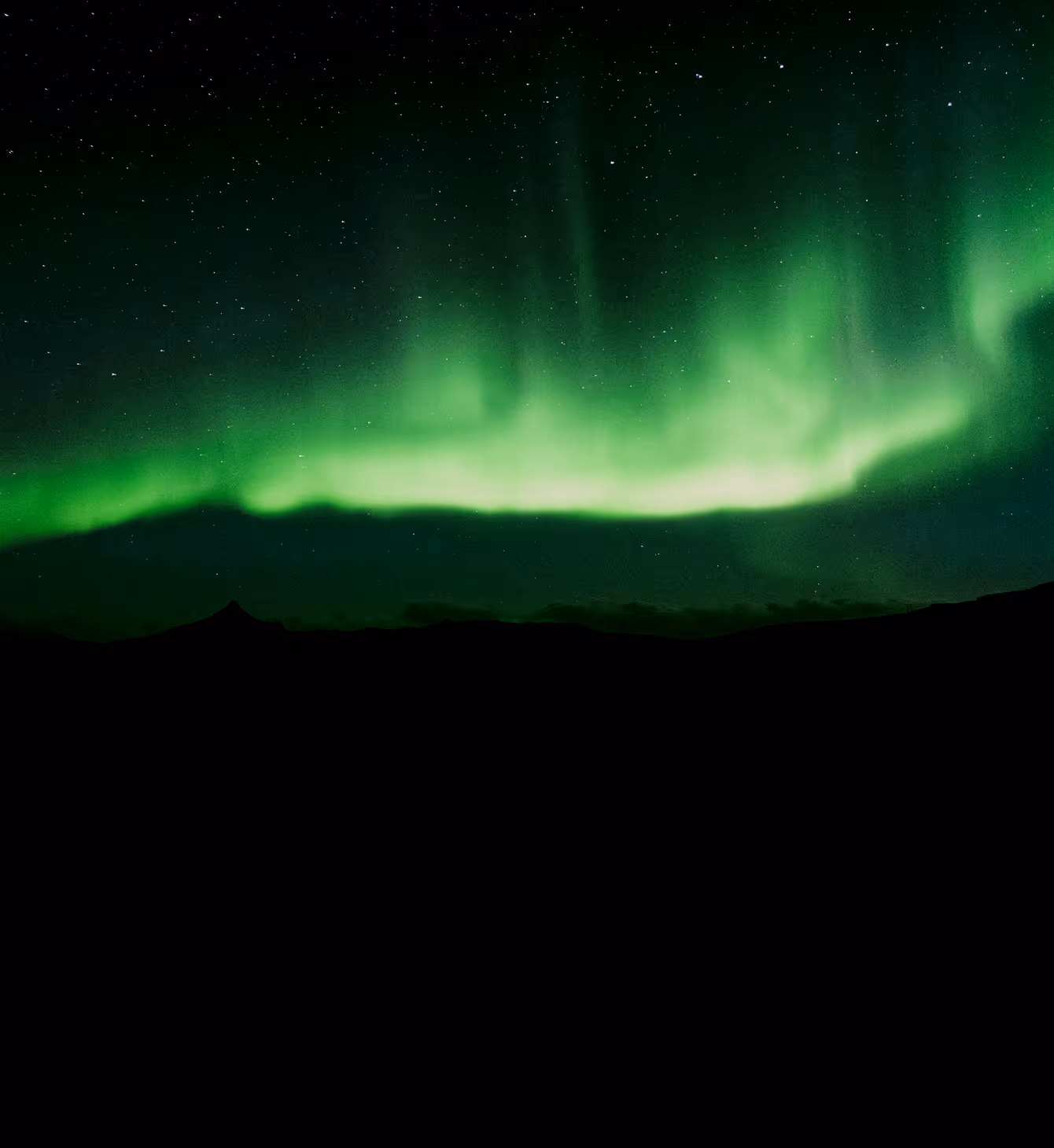 Green northern lights glowing above dark mountain silhouettes under a starry sky.