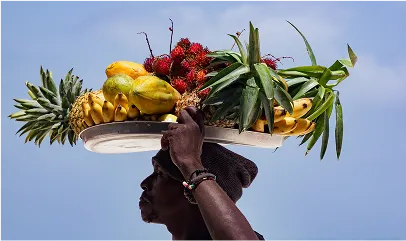 Man carries tray of tropical fruit on his head against blue sky