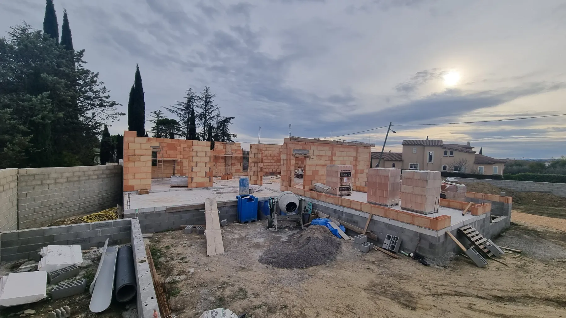Maison individuelle en brique en cours d’élévation entourée de cyprès