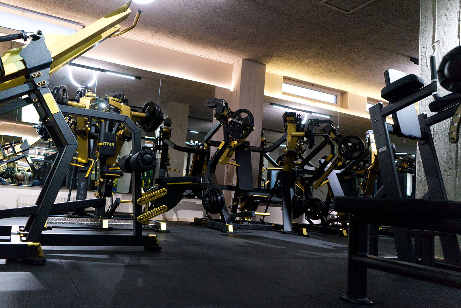 Fitnessstudio mit schwarzen und goldenen Krafttrainingsgeräten vor einem großen Spiegel.