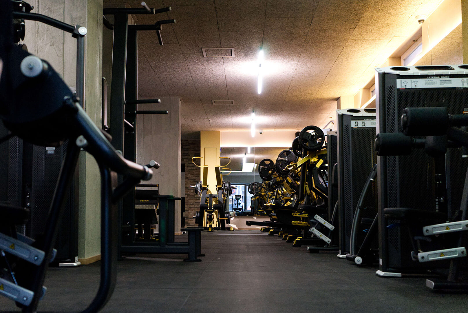 Innenansicht eines Fitnessstudios mit Geräten zum Krafttraining, Gewichten und Spiegeln an der Wand.