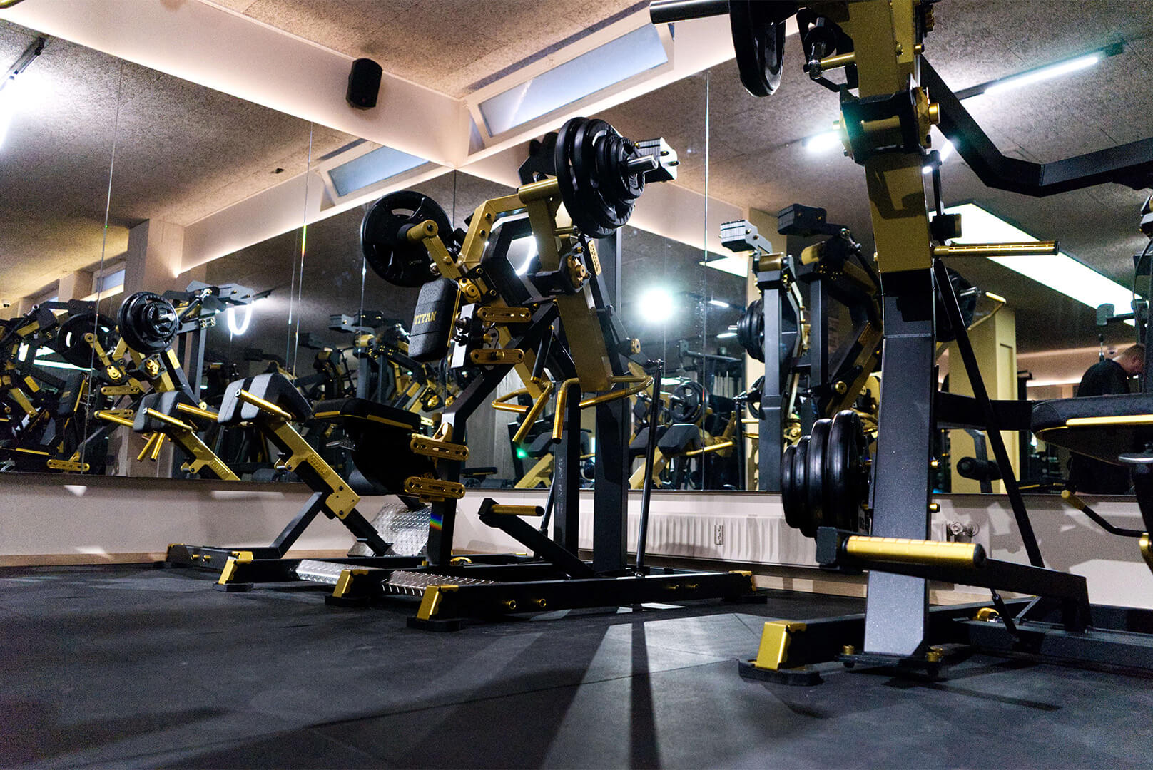 Leerer Fitnessraum mit Krafttrainingsmaschinen in Schwarz und Gelb vor Spiegelwand.