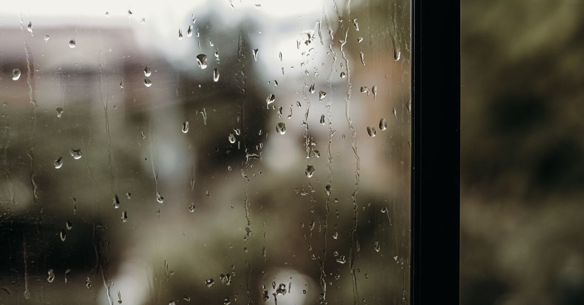 Close-up of raindrops on a window with a blurred view outside, creating a moody atmosphere.