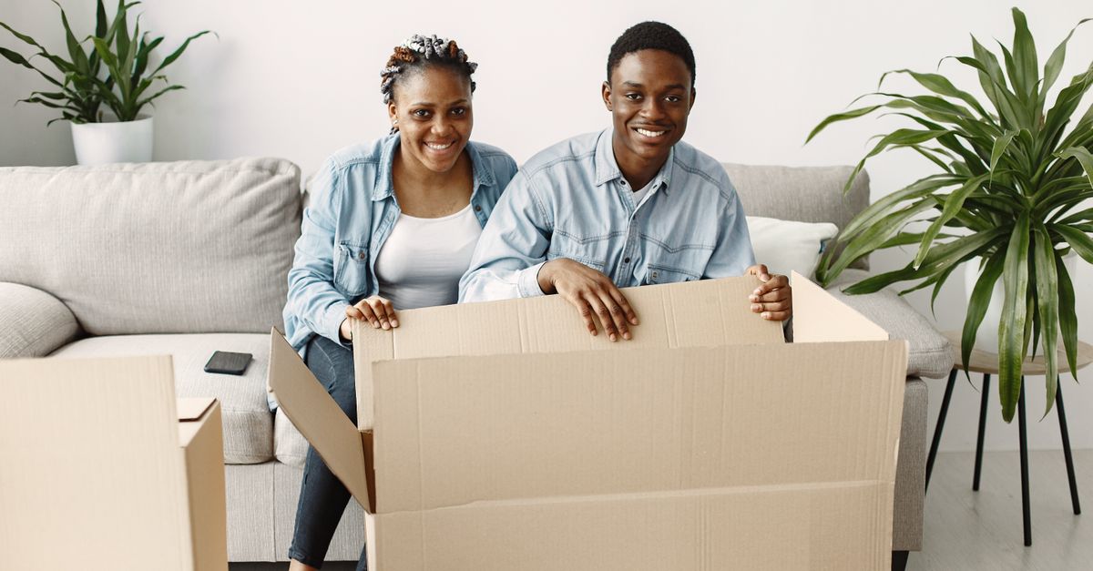 A young couple smiling while unpacking boxes in their living room, creating a joyful moving experience.
