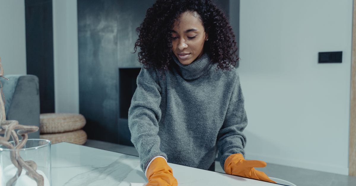 Woman wearing gloves wipes a table in a cozy modern living room.