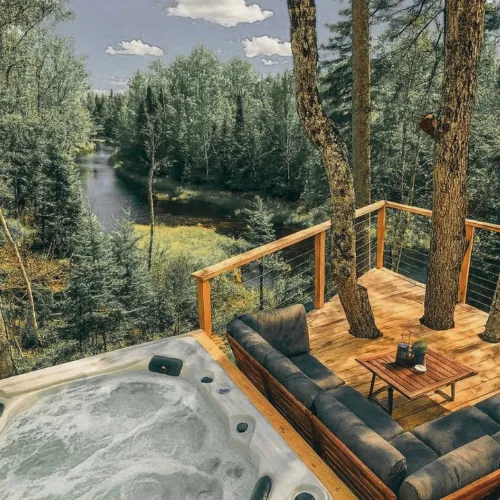 Hot tub on a wooden deck among tall pines, overlooking a river