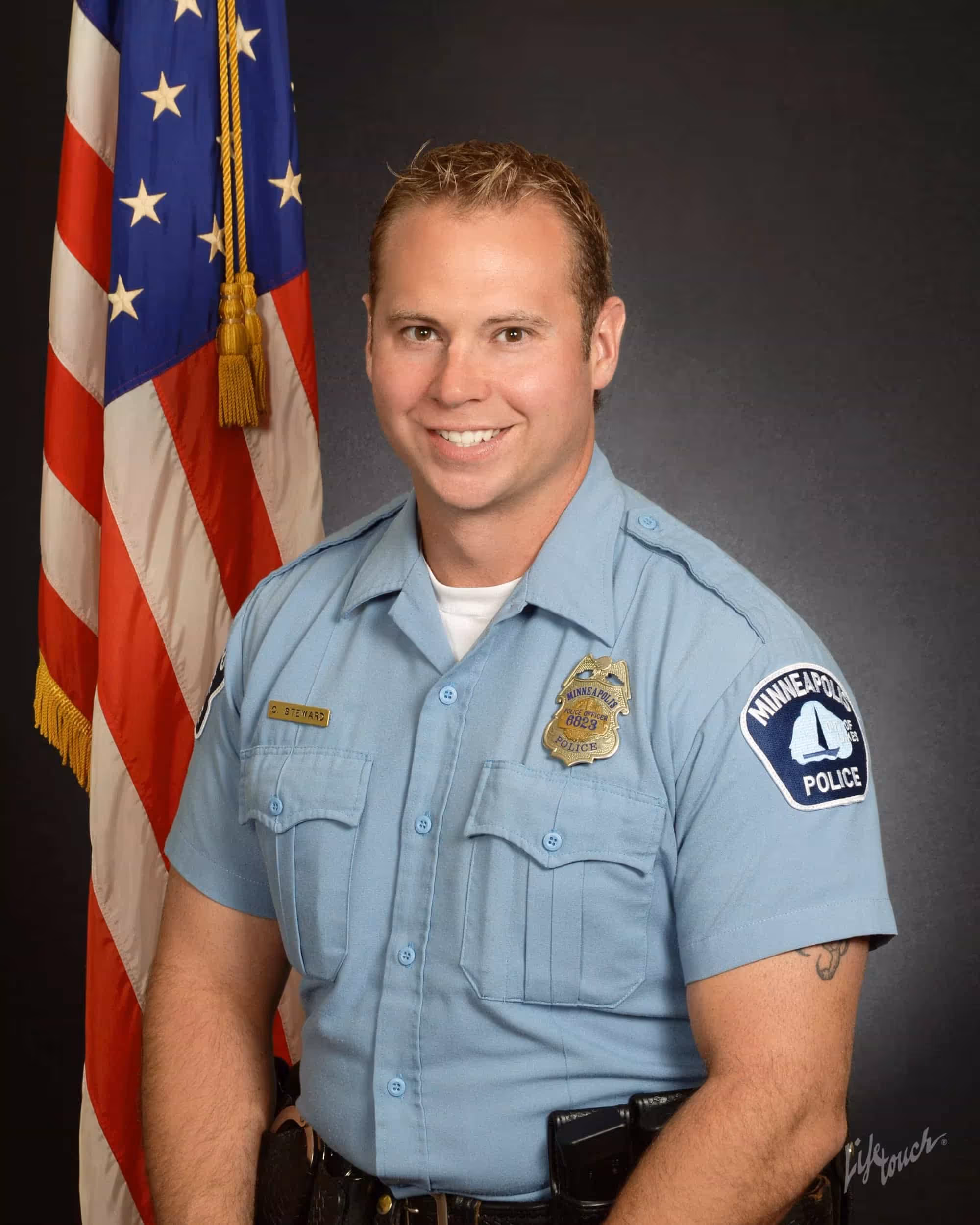 Chris Steward sitting in front of American Flag dressed in Minneapolis Police uniform.