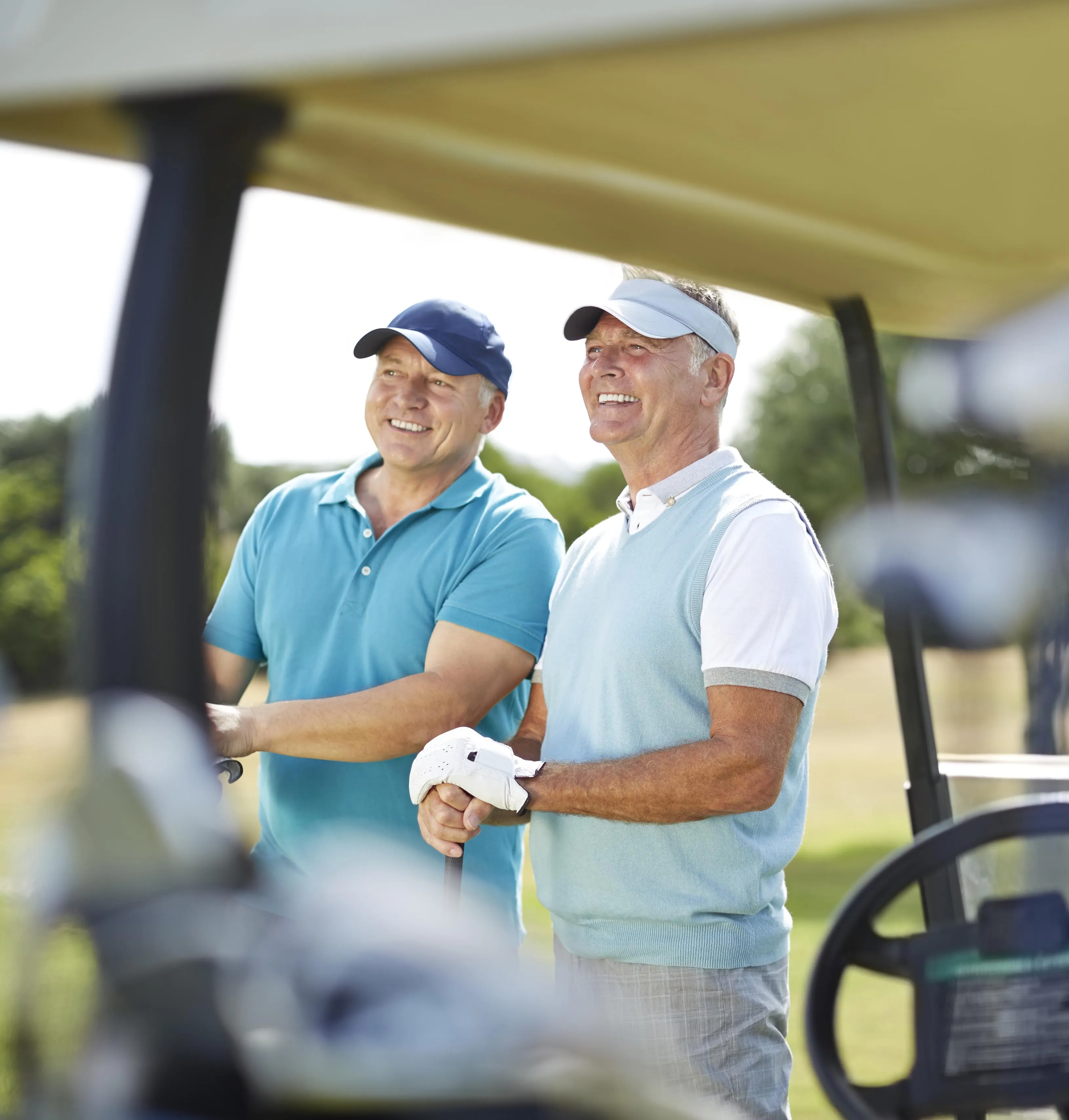 Two middle-aged men smiling and standing next to a golf cart on a sunny golf course.