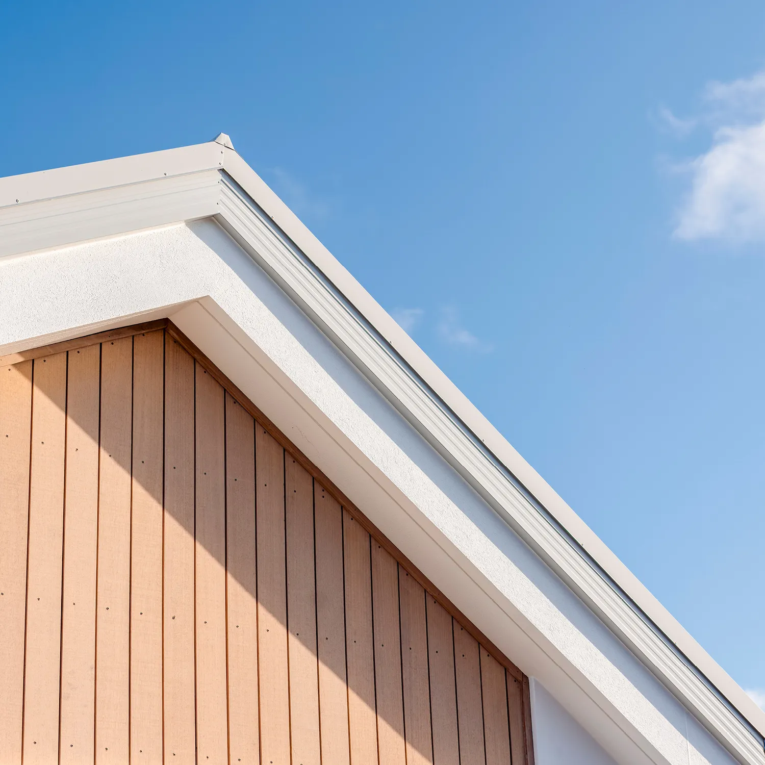 Close-up of a building corner with light wood vertical paneling, white trim, and a clear blue sky background.