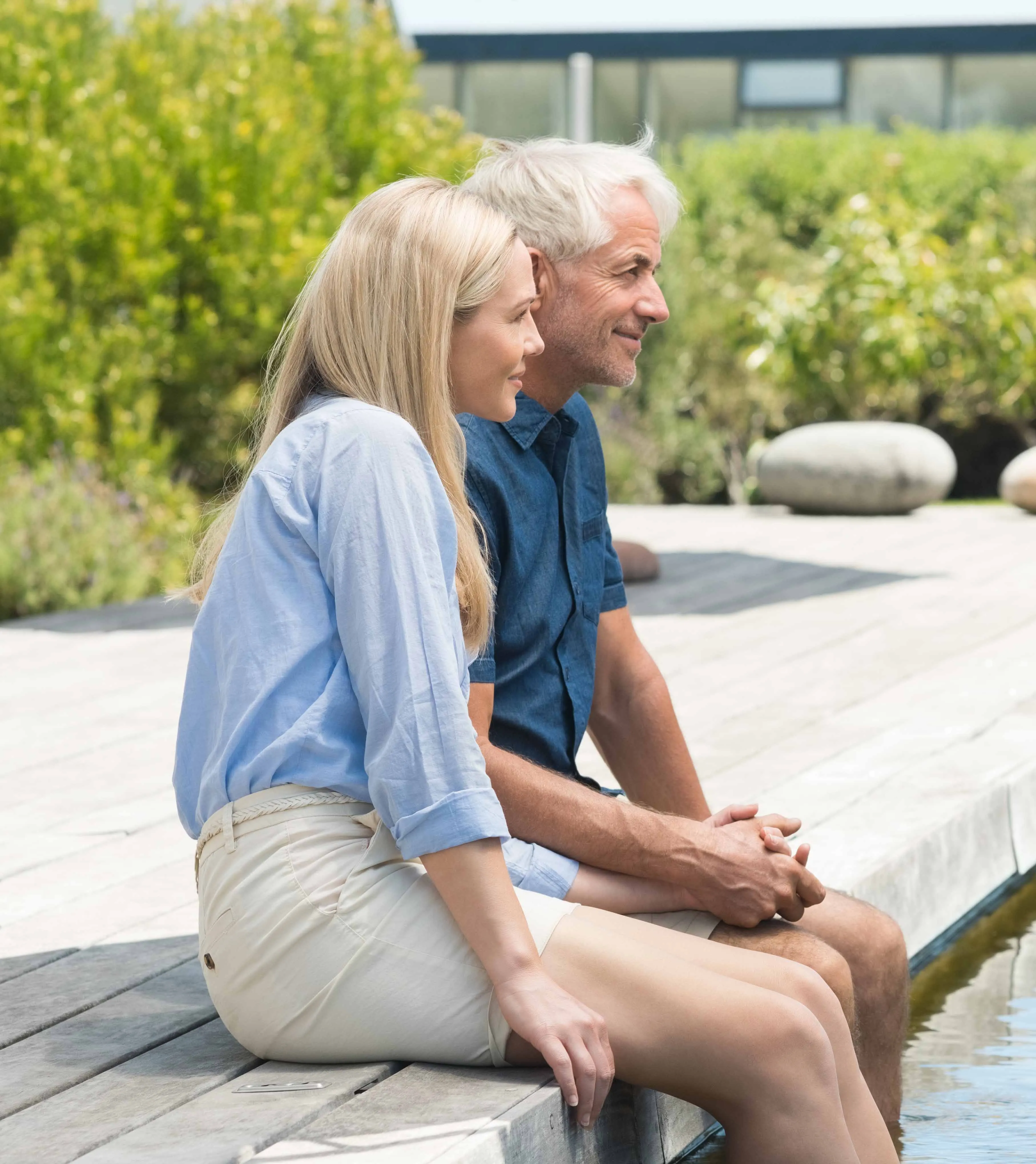over 55 man and women sitting side by side on a wooden dock by the water, smiling and looking ahead.
