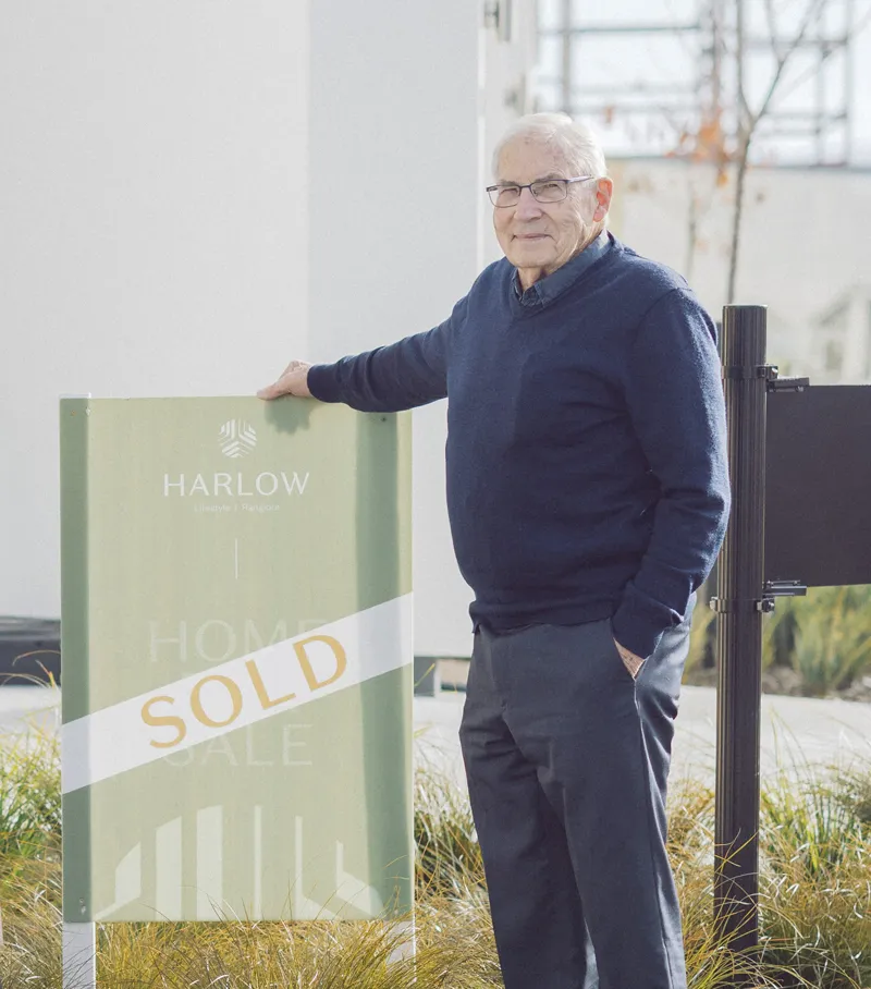 Gerrad the first resident standing next to a sign that reads Harlow Home Sale with a sold banner.