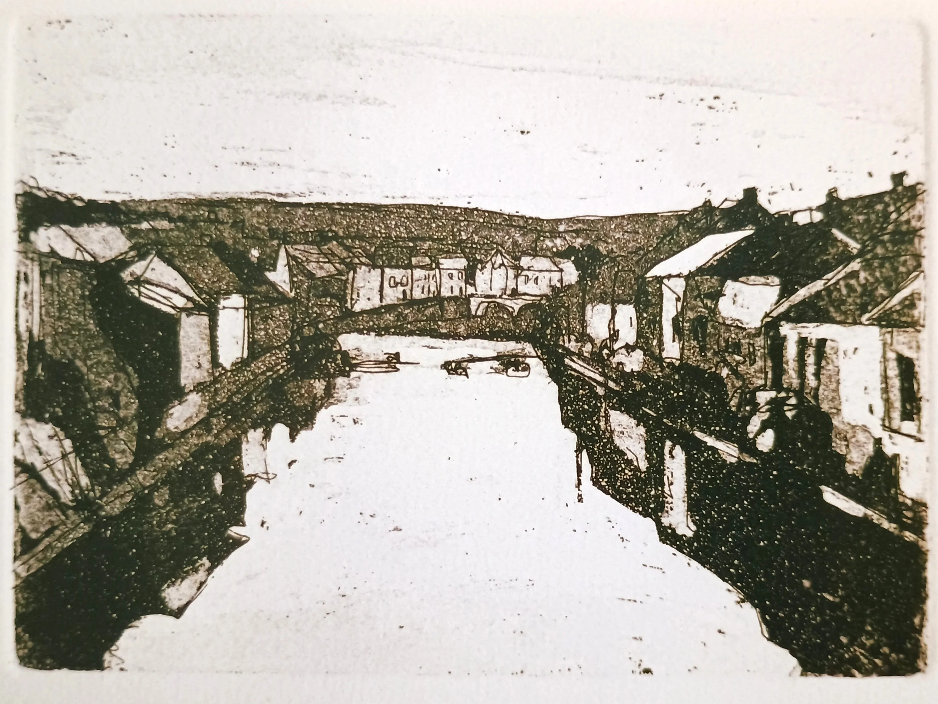 Vintage aquatint print of a village river scene with houses lining both banks and a bridge in the background.