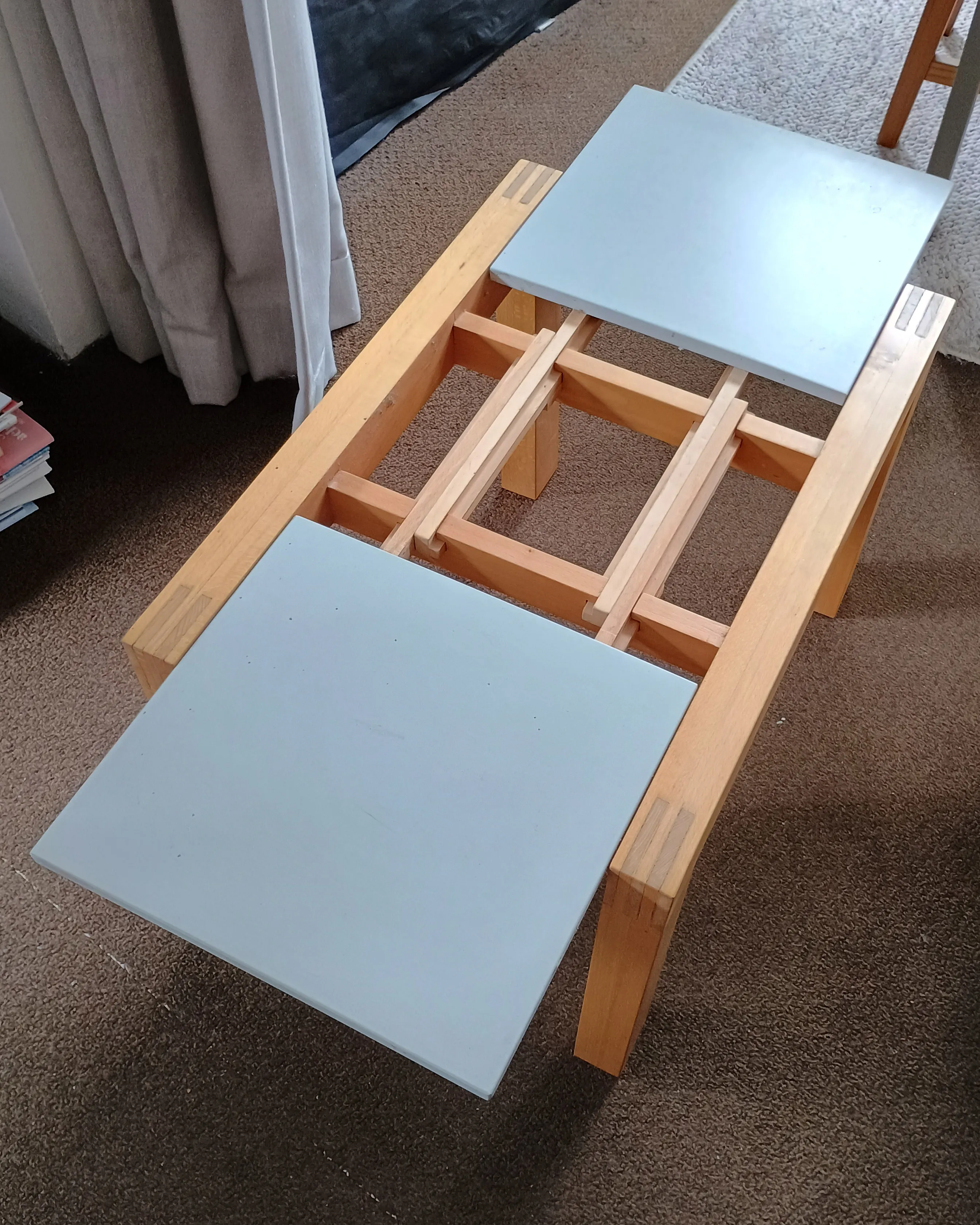 Wooden extendable table with blue panels partially pulled apart showing the sliding mechanism.