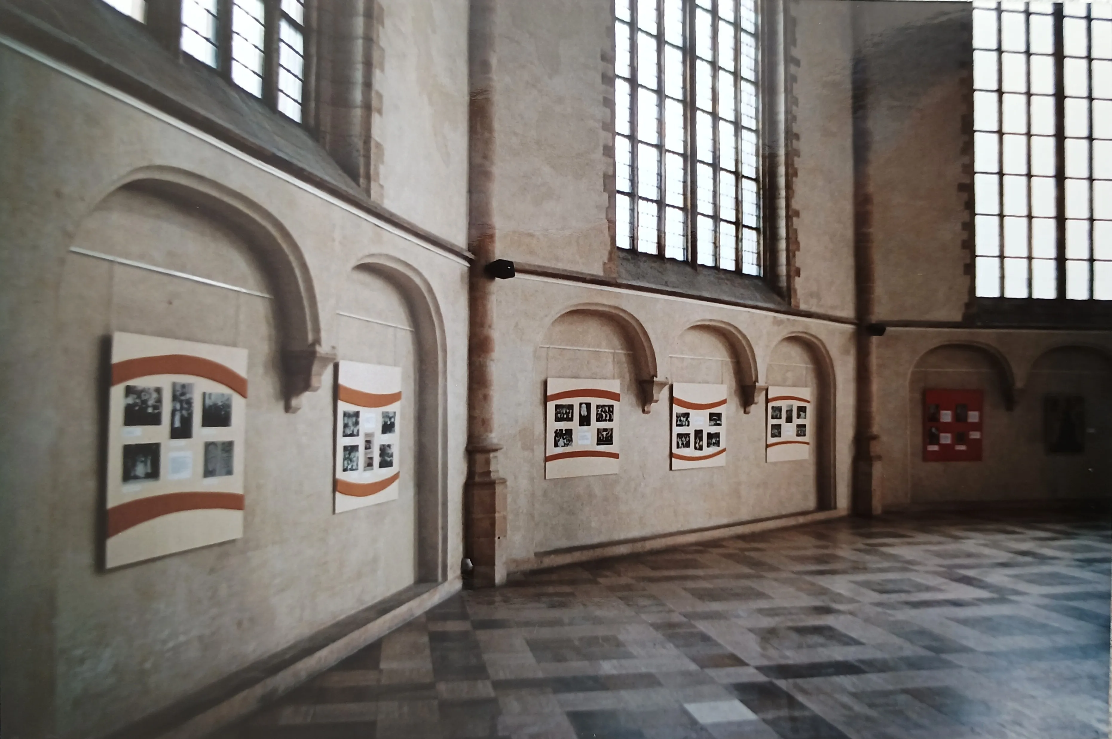 Interior of a historic building with large arched windows and walls displaying photo exhibition panels.