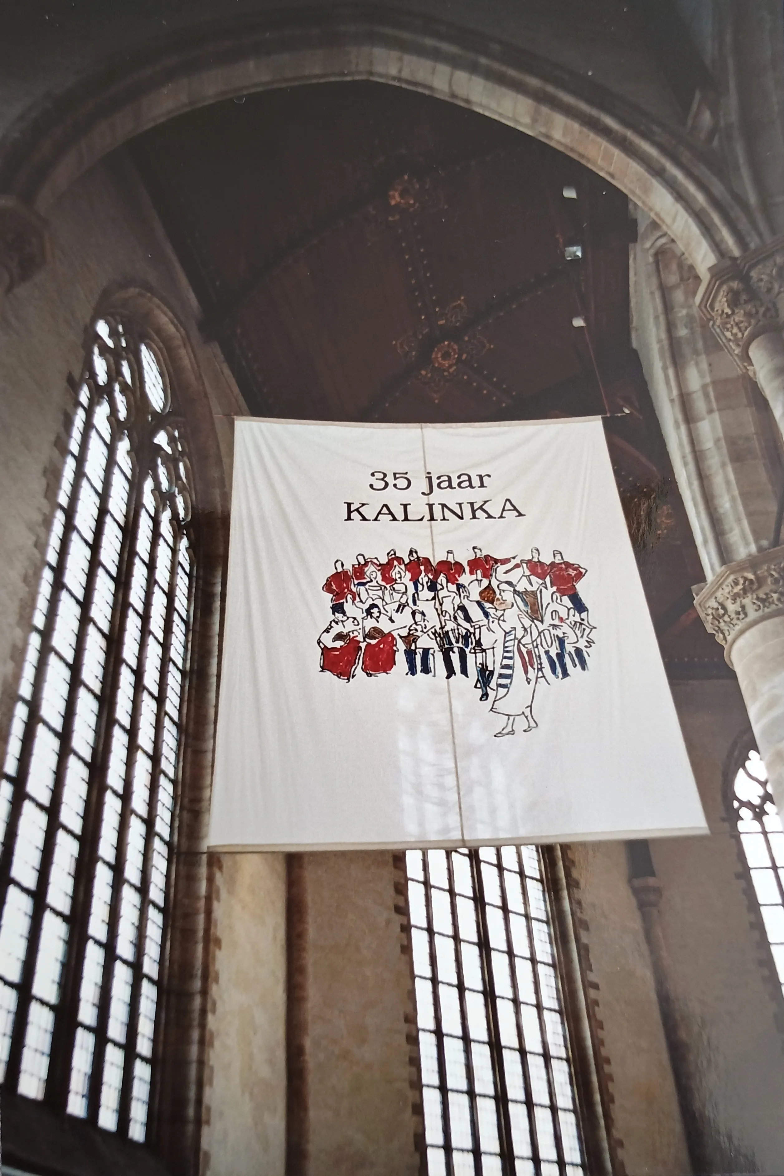 Large banner hanging inside a historic church with text '35 jaar KALINKA' and an illustration of a group of people in colorful clothing.