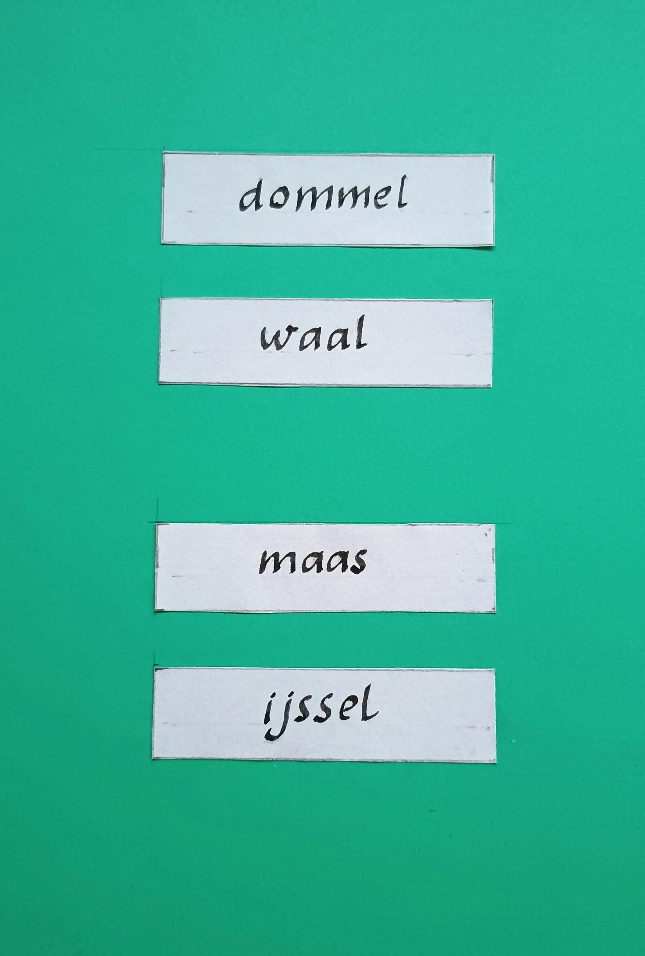 Four white paper strips with black handwritten names dommel, waal, maas, and ijssel on a green background.