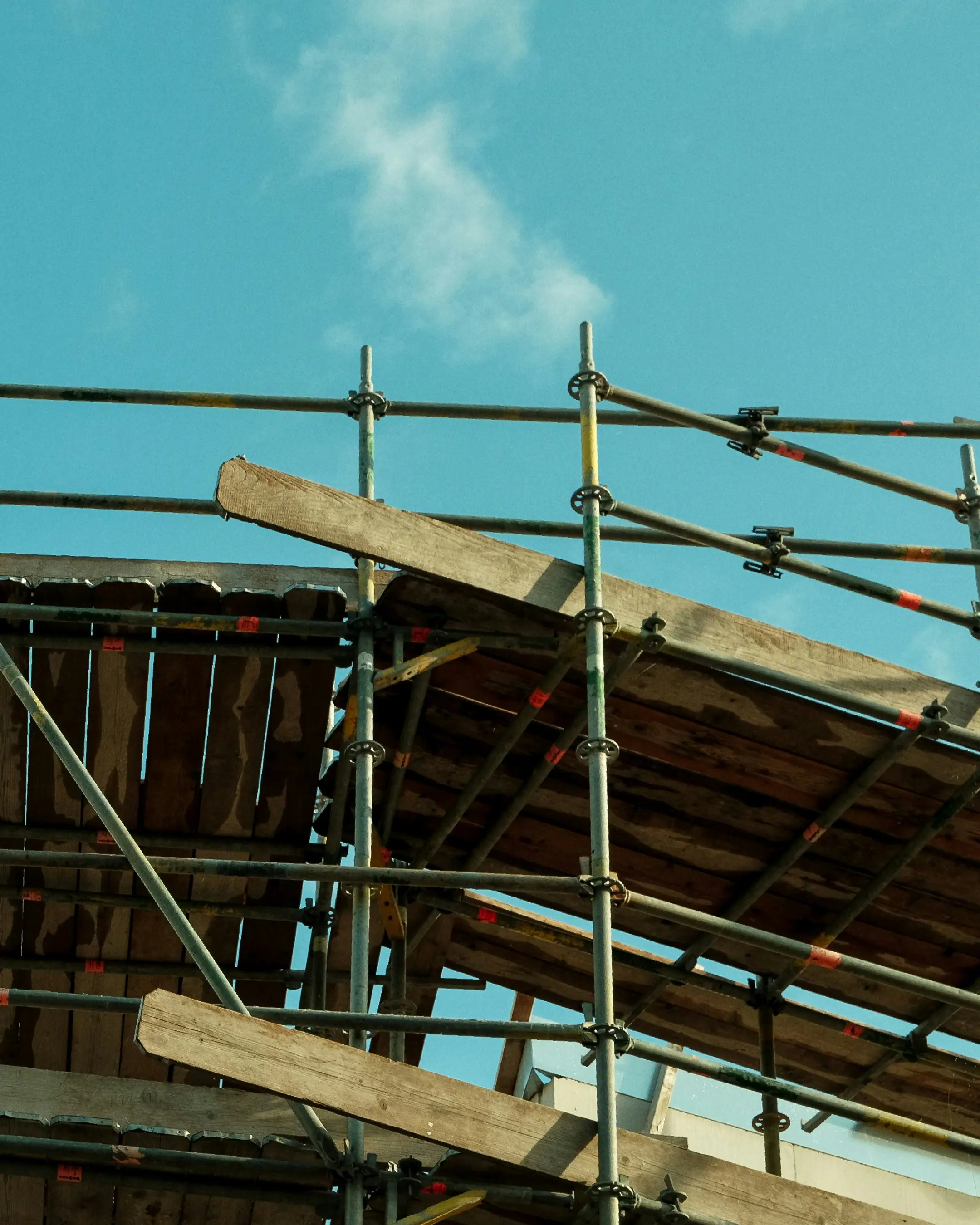 Dettaglio di un ponteggio metallico in cantiere con assi di legno trasversali sotto un cielo azzurro terso.