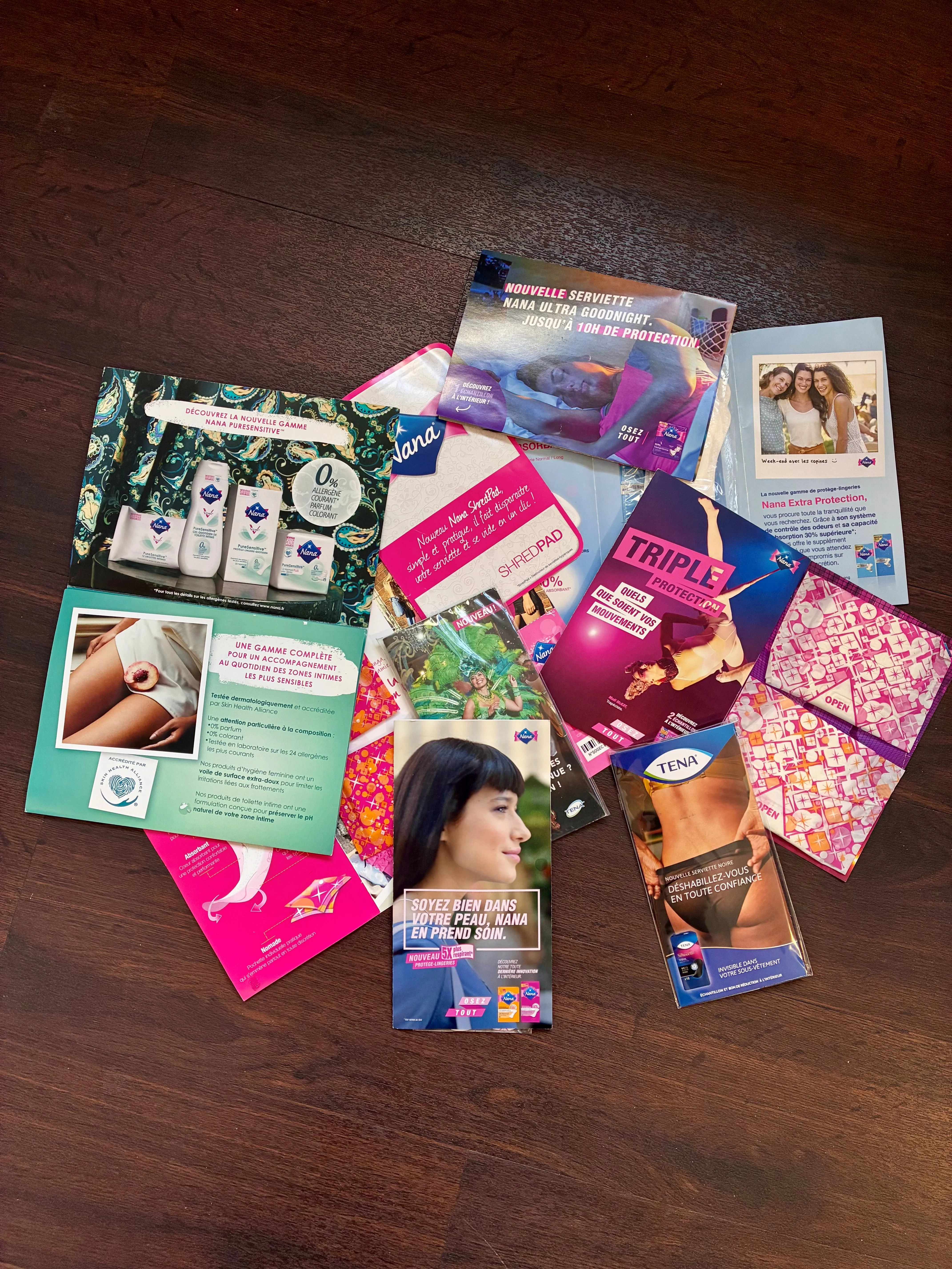 Divers dépliants publicitaires pour produits d'hygiène féminine Nana et TENA posés sur une surface en bois foncé.