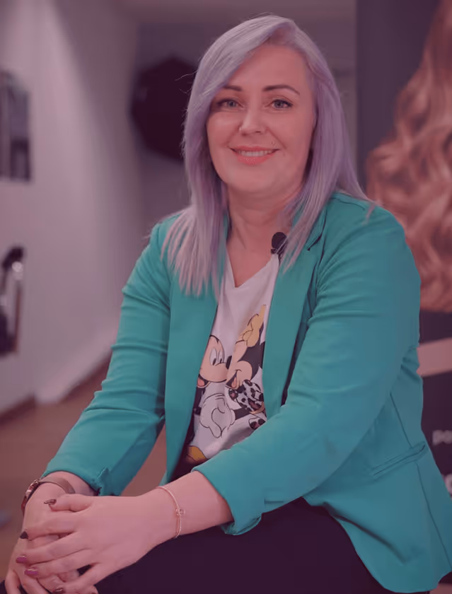Frau mit lila Haaren und grünem Blazer lächelt in Friseursalon.