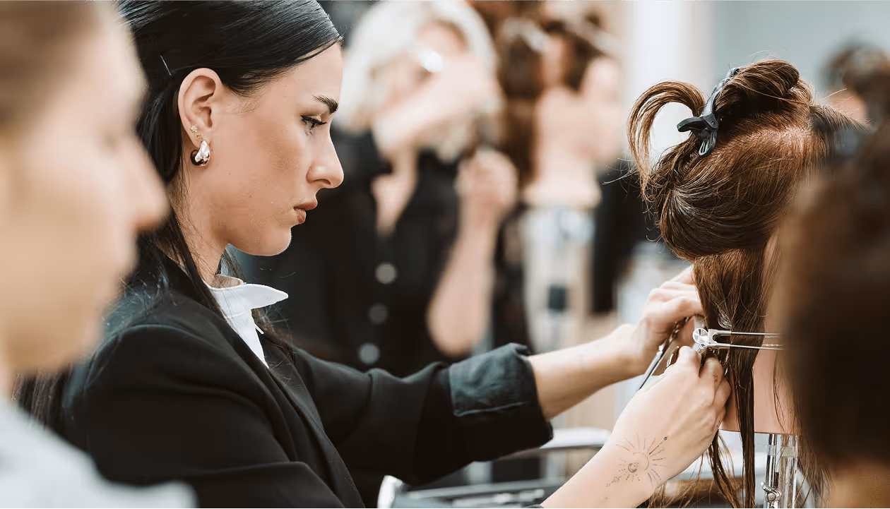 Stylistin schneidet Haare in einem Salon, konzentriert arbeitend, umgeben von anderen Friseuren, Fokus auf Präzision.