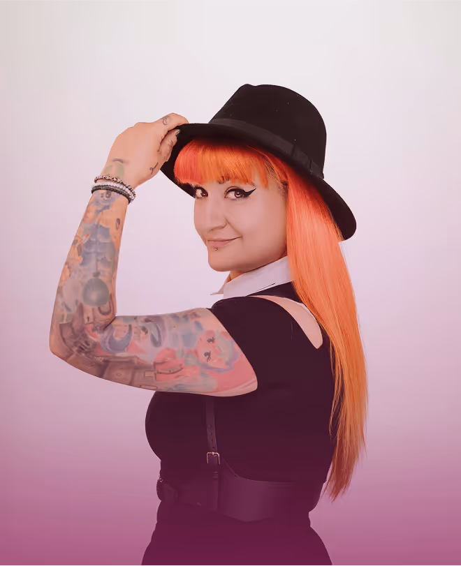 Frau mit rotem Haar, schwarzem Hut und tätowiertem Arm in schwarzem Kleid, lächelt über die Schulter auf pastellviolettem Hintergrund.