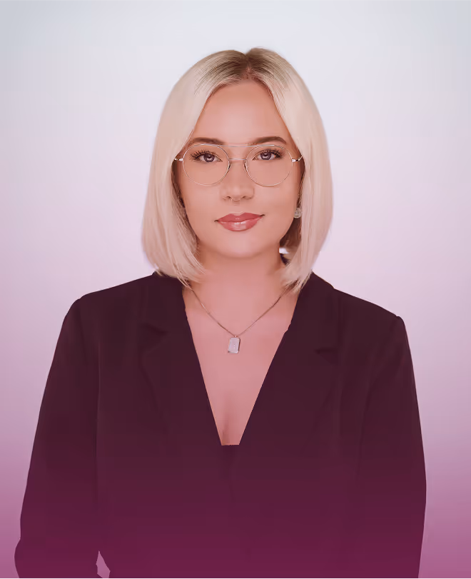 Frau mit blonden Haaren, Brille und schwarzem Blazer vor neutralem Hintergrund.