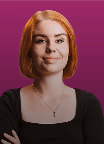 Frau mit kurzen roten Haaren vor lila Hintergrund, trägt schwarzen Pullover und silberne Halskette, schaut lächelnd.