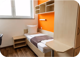 Small bedroom with single bed, beige furniture, orange accent wall, and wood flooring.