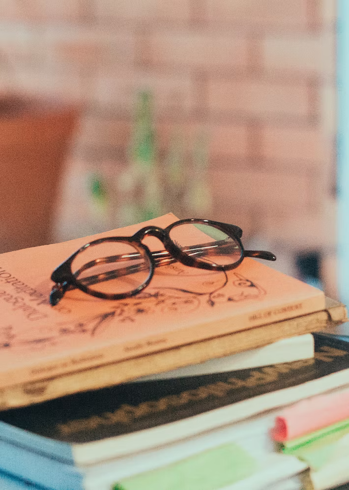 Black round eyeglasses resting on top of a stack of books with a blurred background.