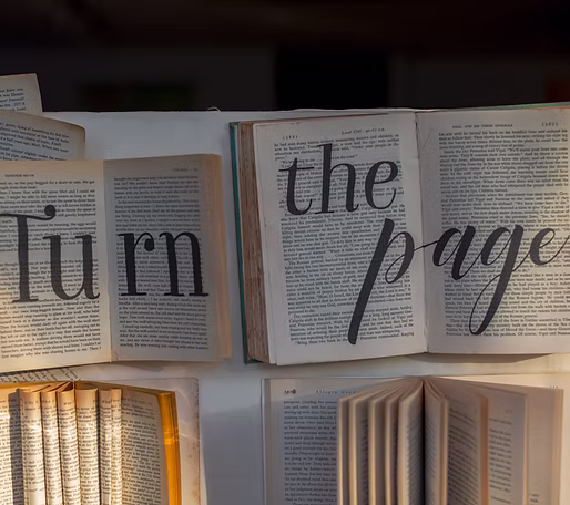 Open books laid out on a surface with the text 'turn the page' overlaid in large, stylized letters.