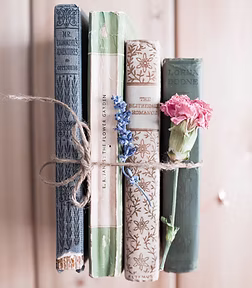 Four vintage books tied together with twine, decorated with pink and blue flowers on a wooden surface.
