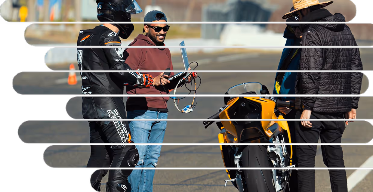 Damon team members standing beside a yellow electric motorcycle during testing, one rider in full gear and others holding diagnostic tools.