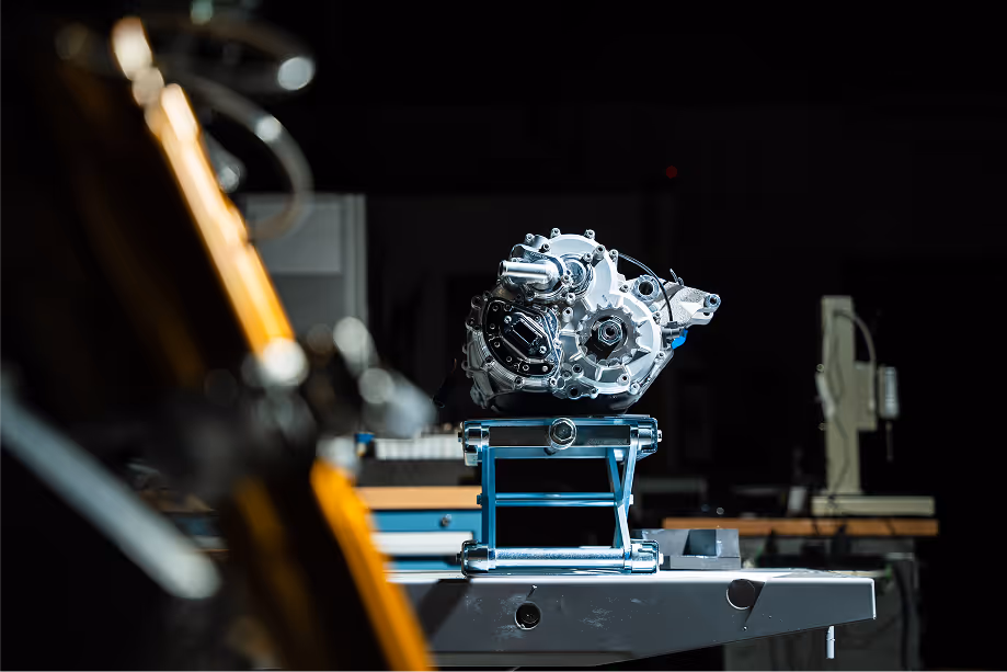 High-performance motorcycle powertrain displayed on a stand in an engineering lab, with robotic equipment in the foreground.