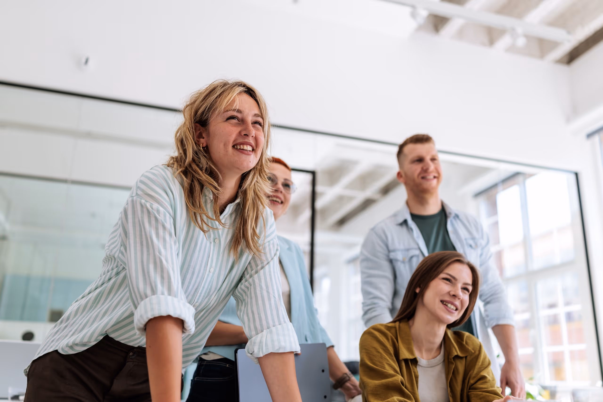 Four young professionals smiling and engaged in a bright modern office setting.