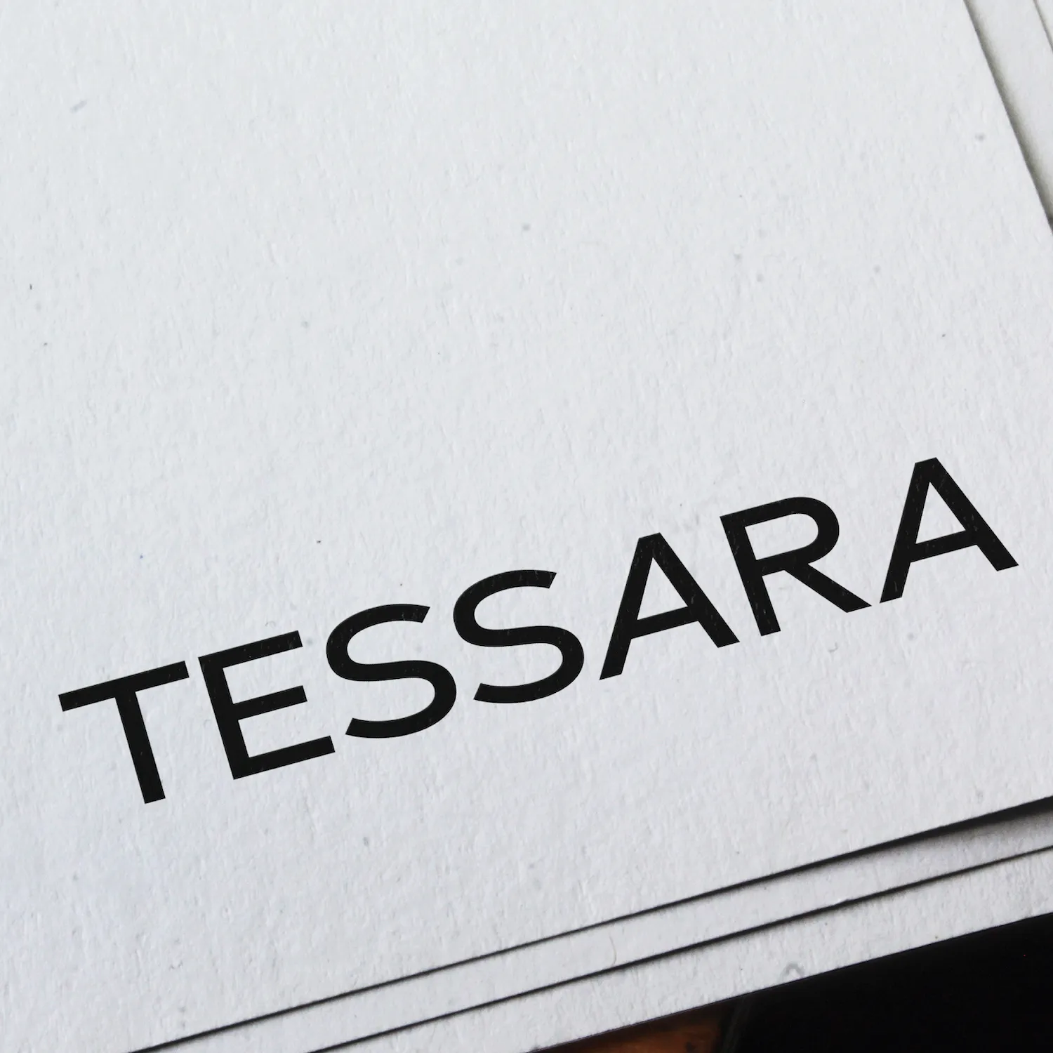 Close-up of a white paper card corner displaying the word 'TESSARA' in bold black letters.