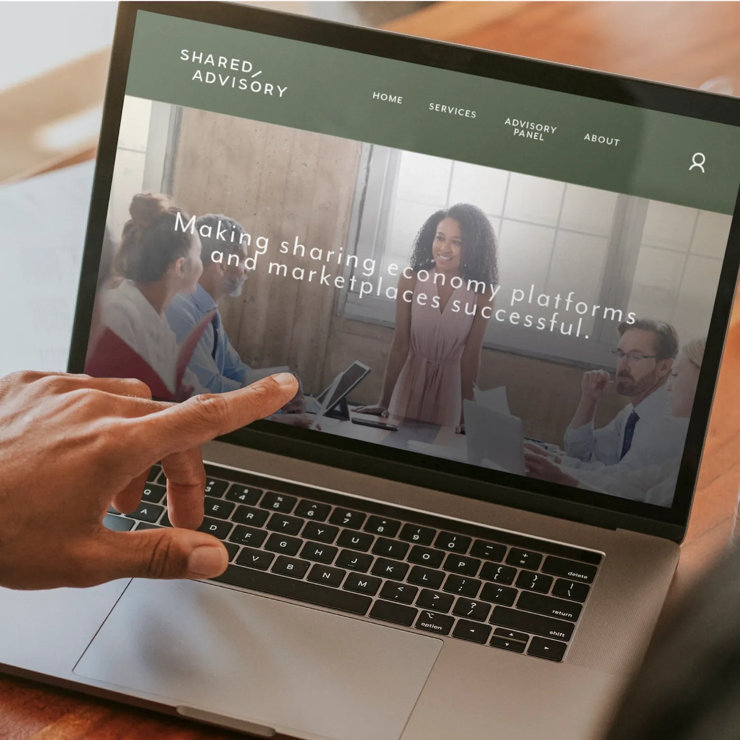 Hand pointing at a laptop screen showing the Shared Advisory website with a group meeting photo and text about making sharing economy platforms successful.