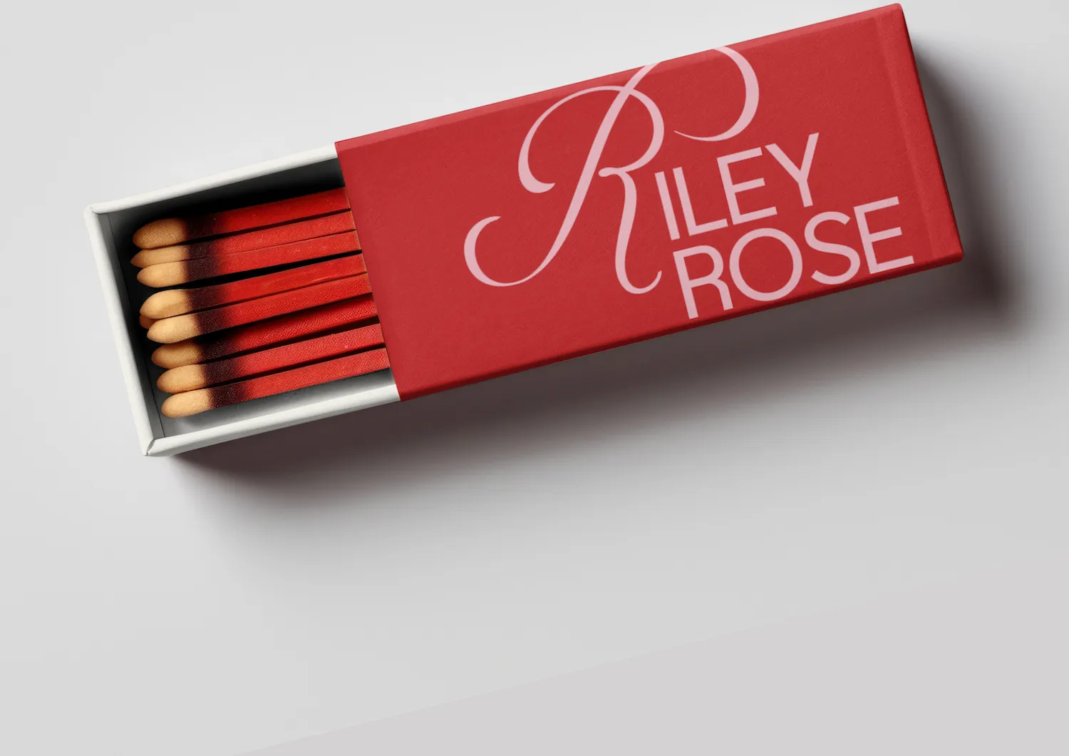 Open red matchbox labeled Riley Rose with red matches inside on a white surface.