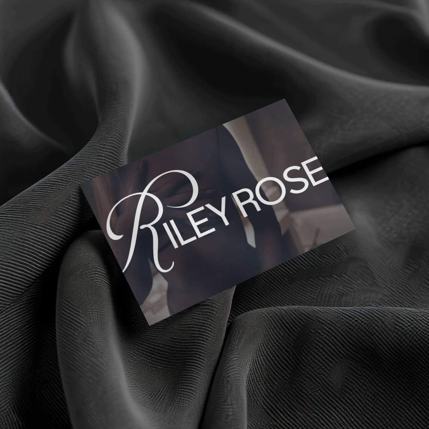 Business card with a blurred image of a person and the stylish text 'RILEY ROSE' placed on black textured fabric.