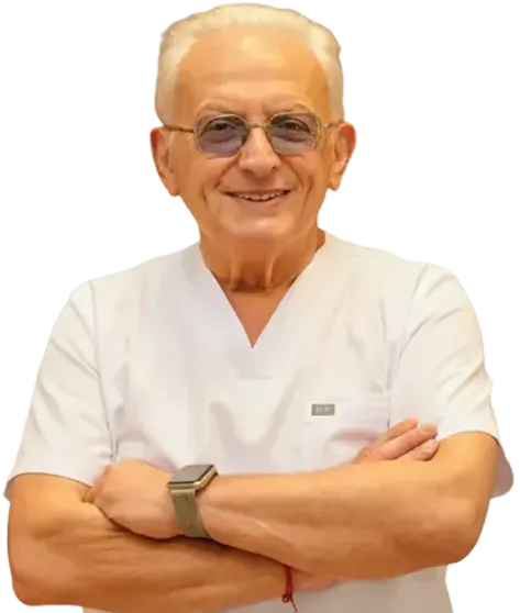 Smiling elderly man wearing glasses and a white medical scrub top with folded arms.