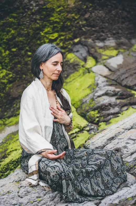 Woman meditating on rocks with hand on chest.