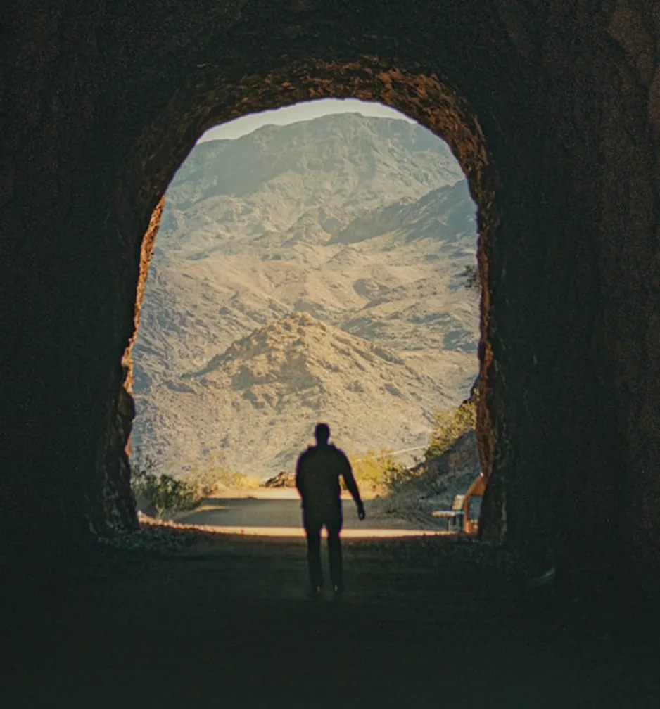 Silhouette of man walking out of a cave toward mountains.