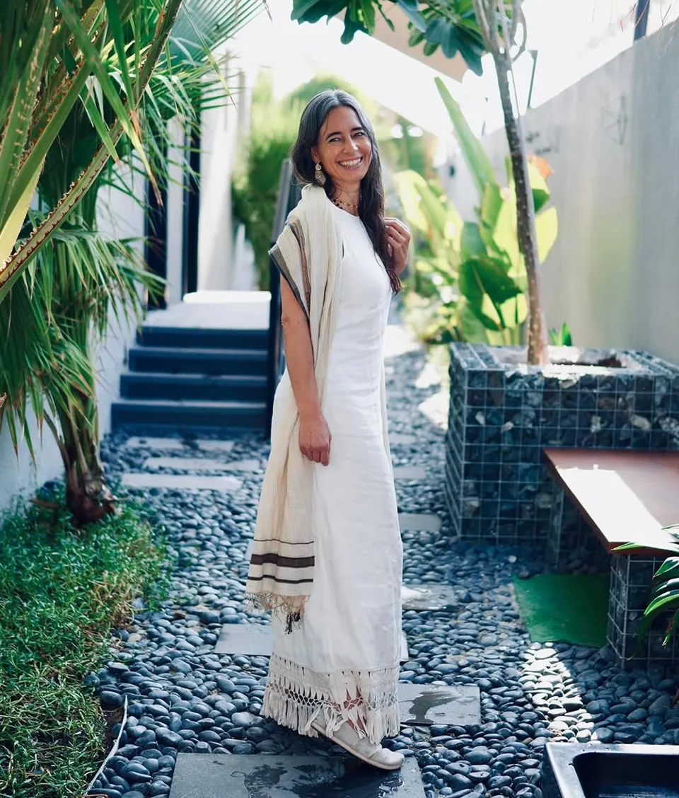Smiling woman in white dress standing in garden path.