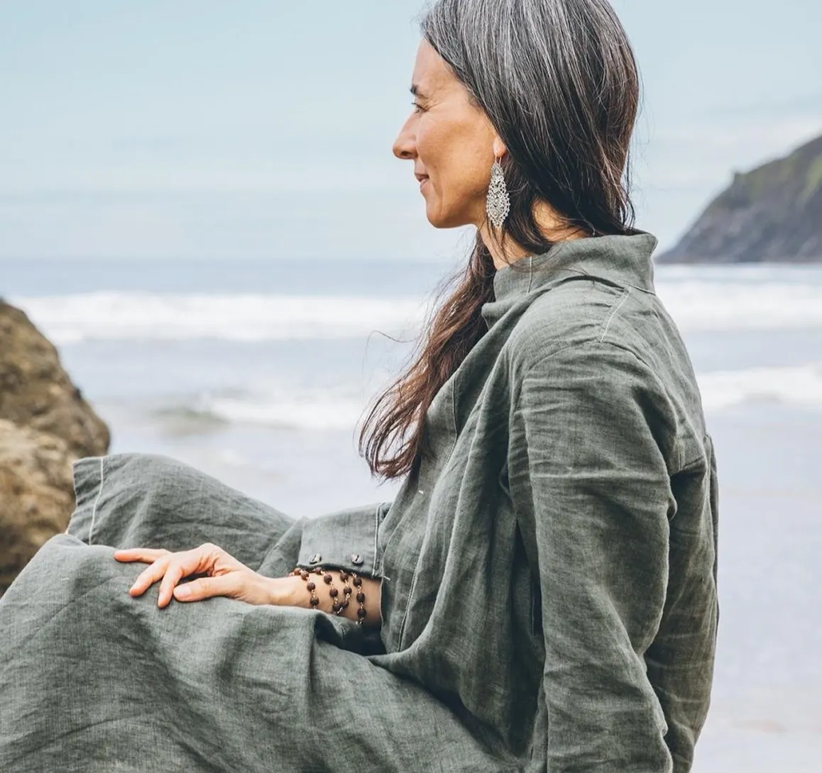 Woman in grey dress sitting by the sea, looking contemplative