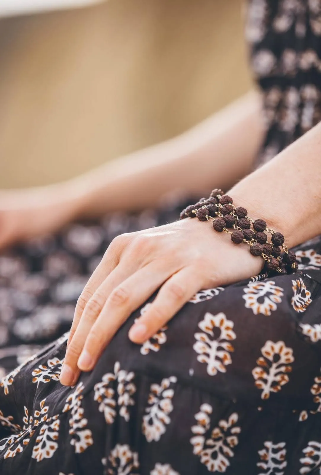 Hand wearing mala beads resting on patterned fabric