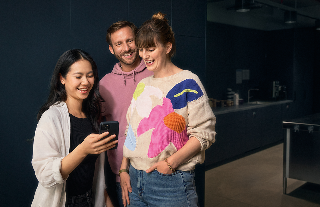Tien Nguyen, Sascha Pres und Christina Kufer gucken gemeinsam auf ein Handy und lachen.