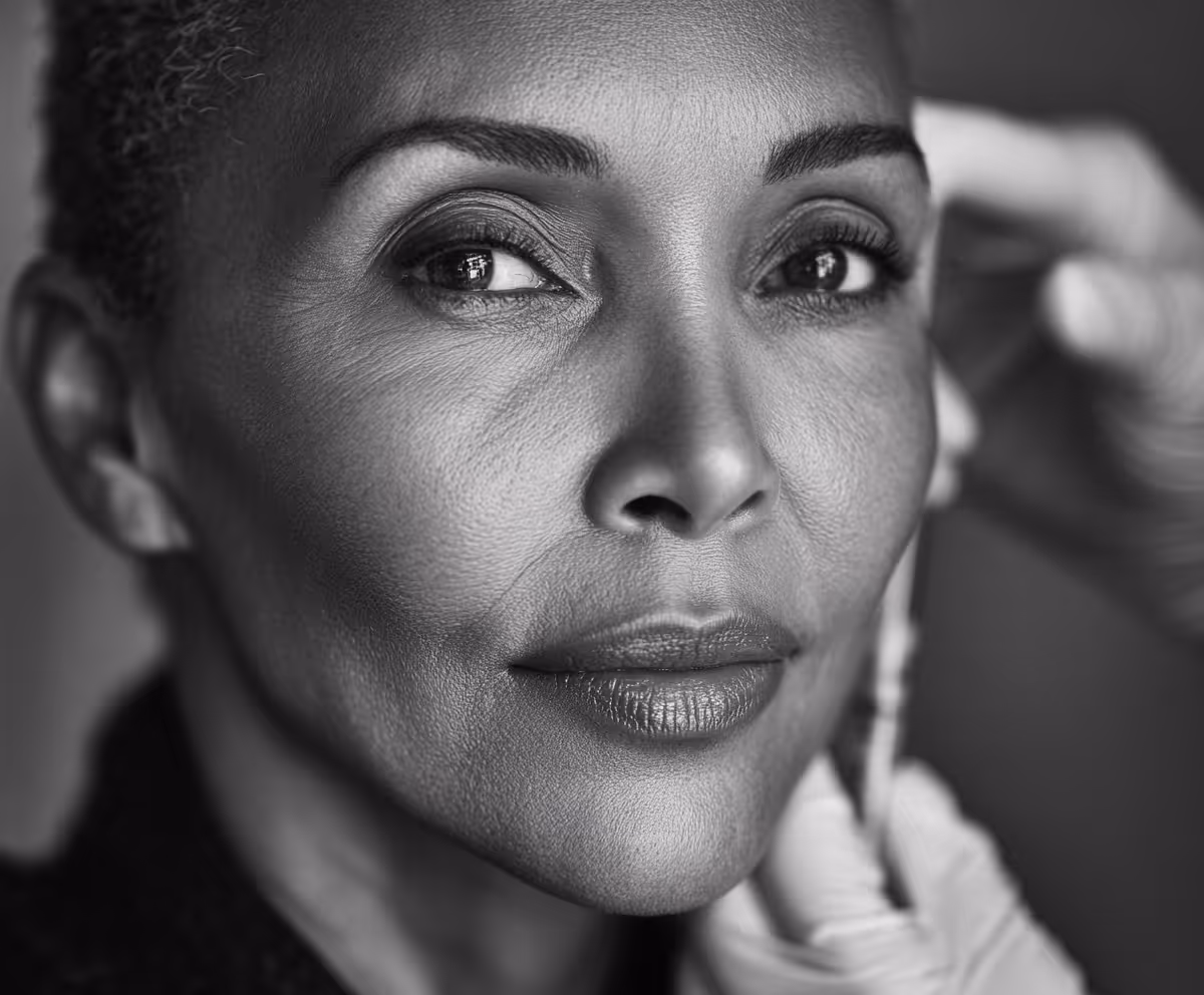 Close-up of a mature woman with gloved hands measuring her face with a tape measure, suggesting a skincare or cosmetic procedure.